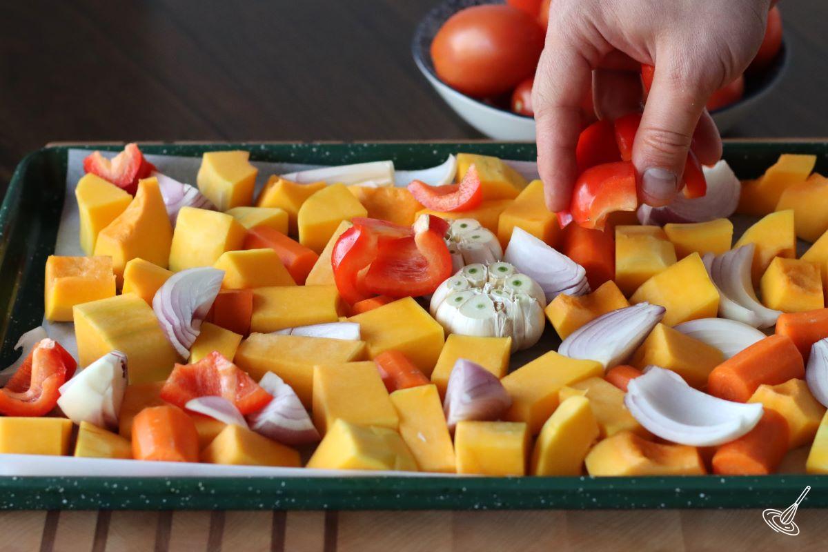 Someone placing chopped vegetables on a baking tray.