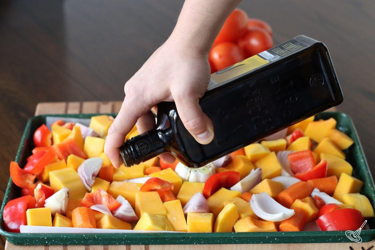 Someone drizzling olive oil over a tray of chopped vegetables.