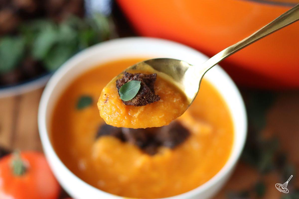 Someone holding up a serving spoon of butternut squash soup. 