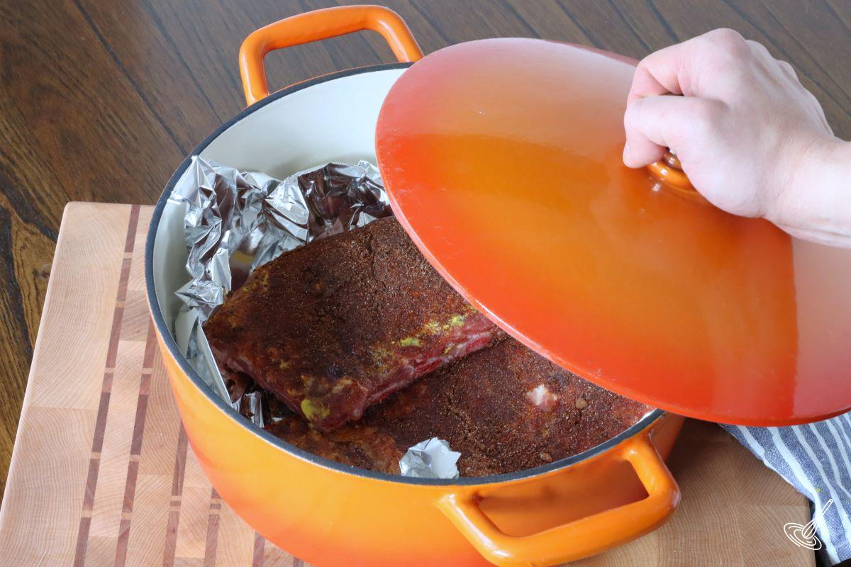 Someone placing the lid on a Dutch oven containing prepared ribs.