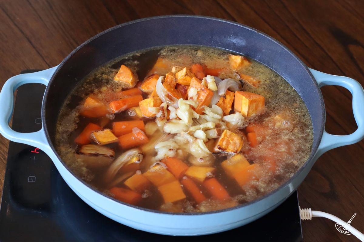 Roasted vegetables cooking in a large pot with broth. 