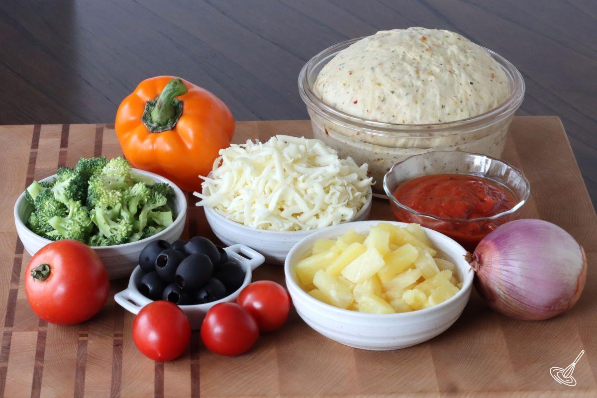Assorted vegetables on a cutting board with a ball of pizza dough.
