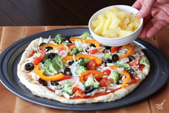 Someone adding pineapple to a veggies pizza.