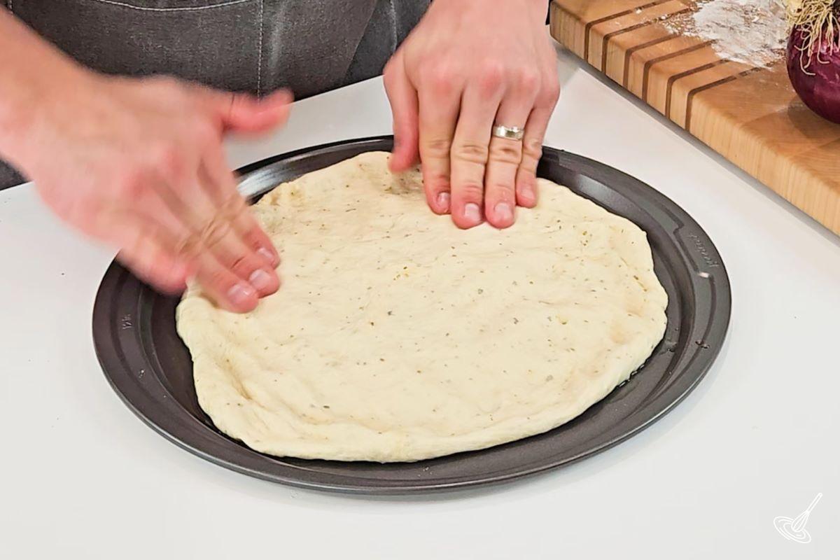 Someone placing pizza dough on a pizza pan. 