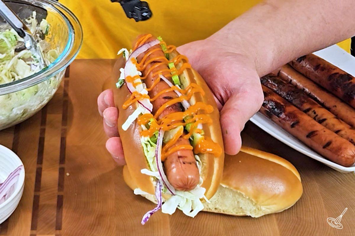 Someone drizzling buffalo sauce on a hot dog.