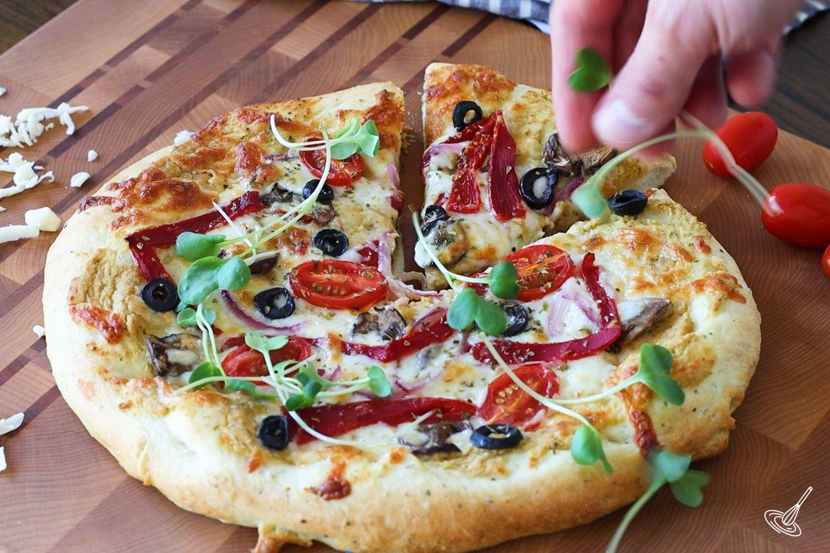 Someone garnishing baked hummus pizza with microgreens. 