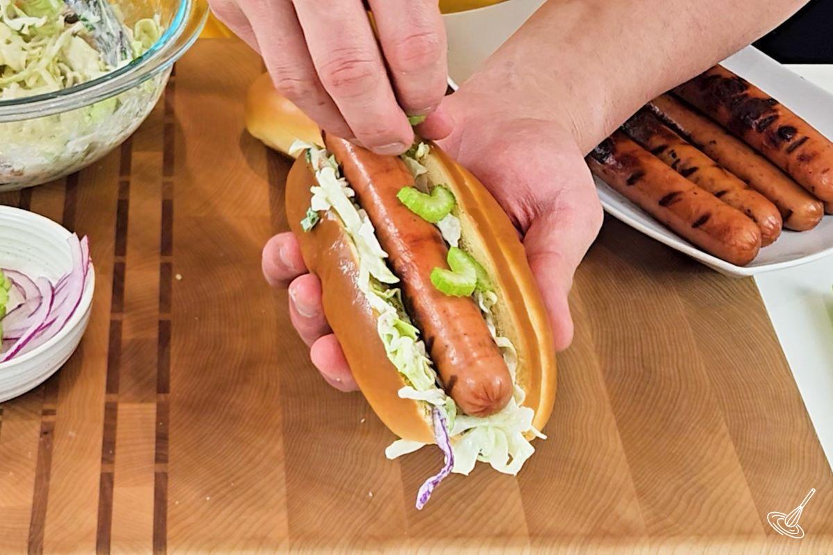 Someone placing celery slices on a hot dog.