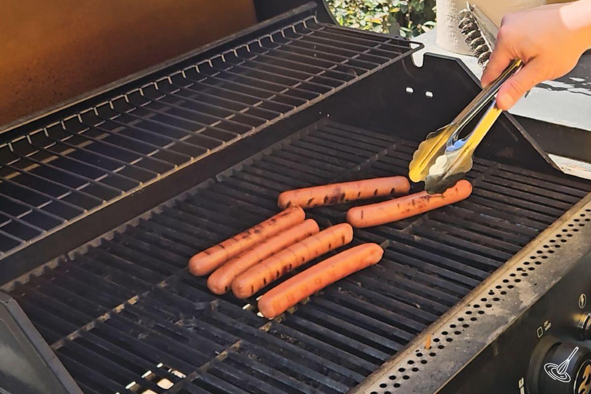 Someone cooking hot dog wieners on the BBQ. 