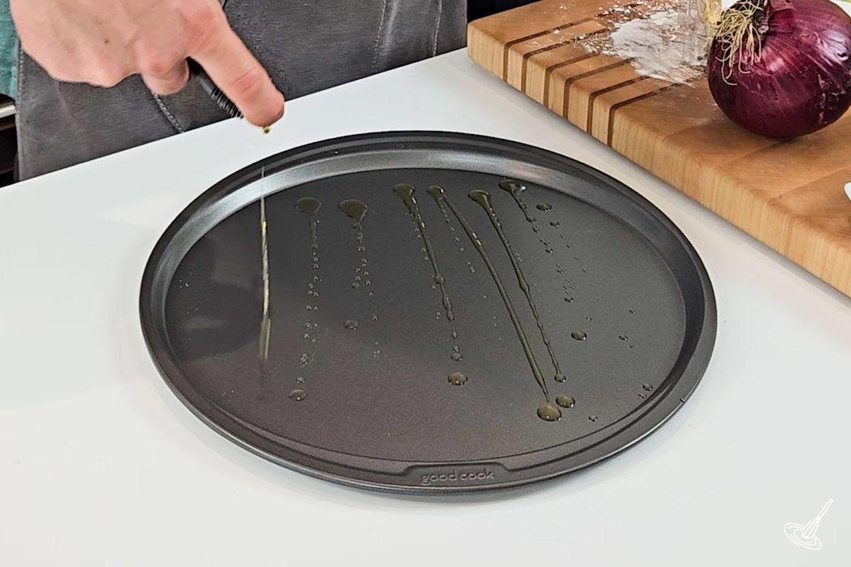 Someone drizzling olive oil on a pizza pan. 