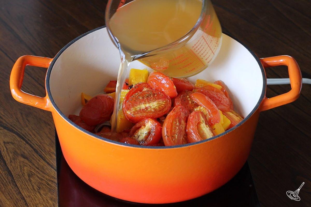 Someone pouring chicken broth in a Dutch oven which contained roasted vegetables.