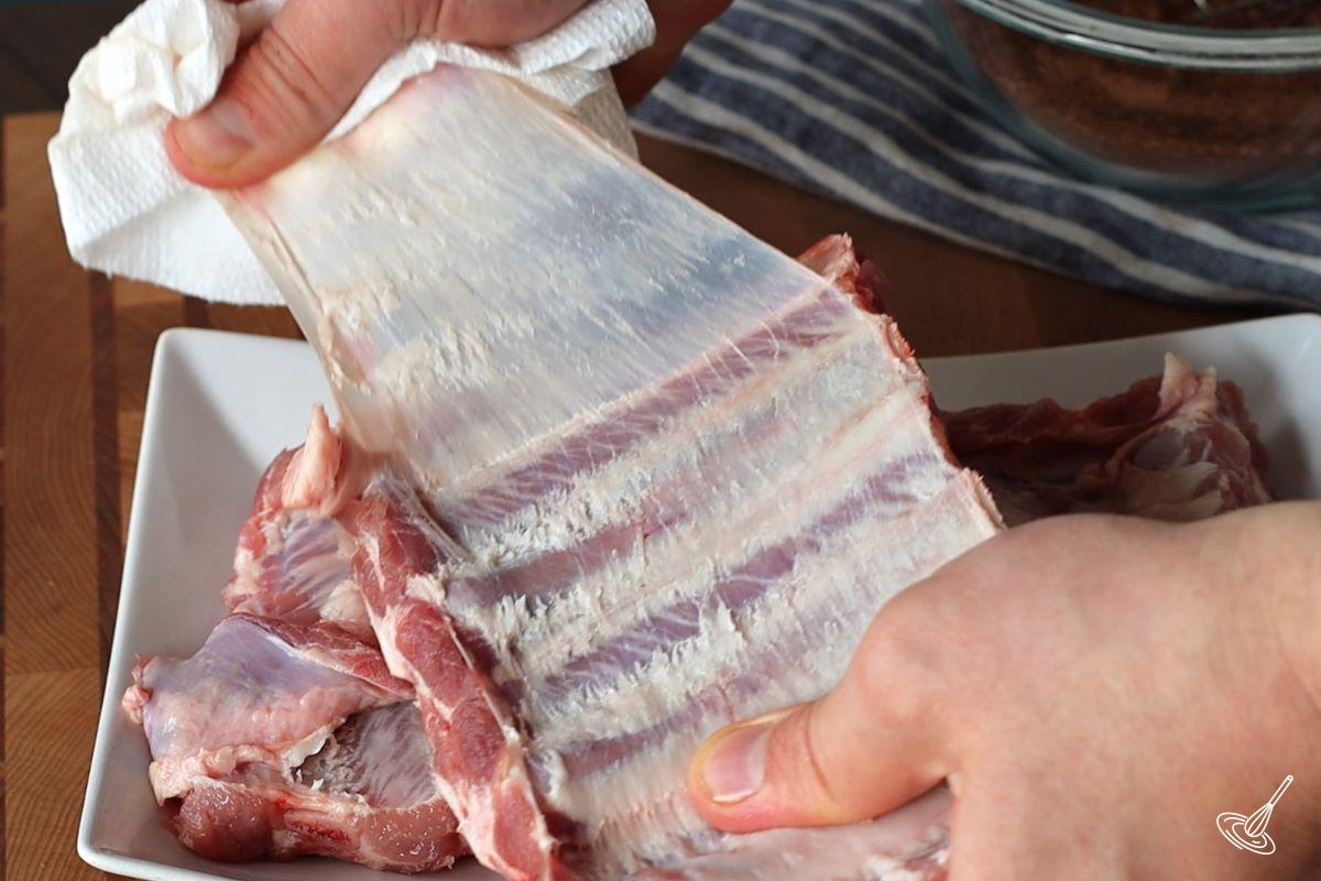 Someone pulling off the membrane off from the back of the rack of ribs.