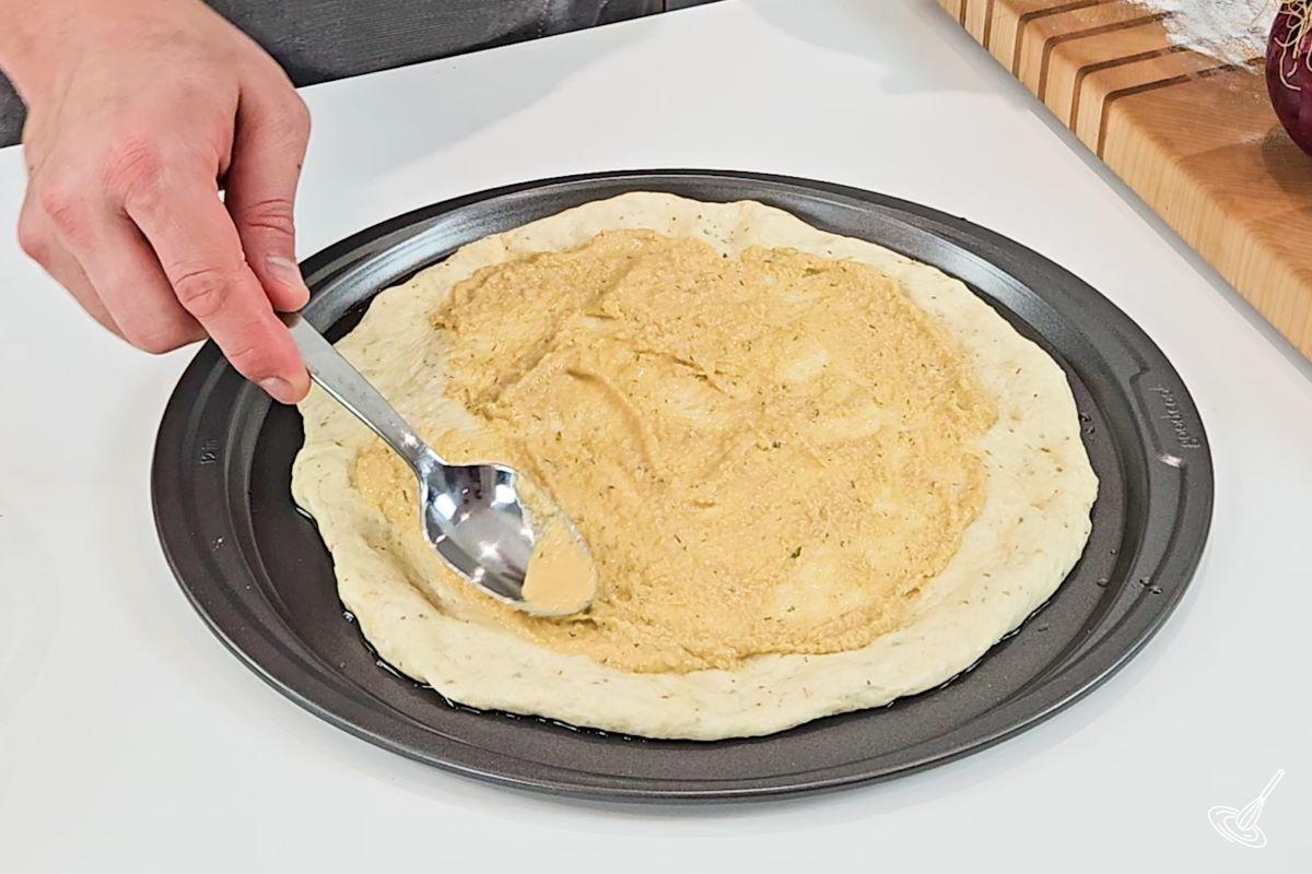 Someone spreading hummus on a pizza crust.