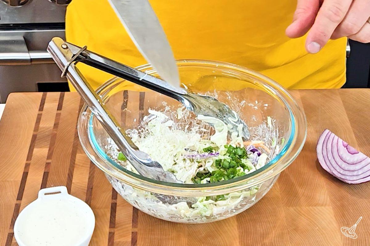 Someone adding sliced green onions in a bowl of coleslaw. 