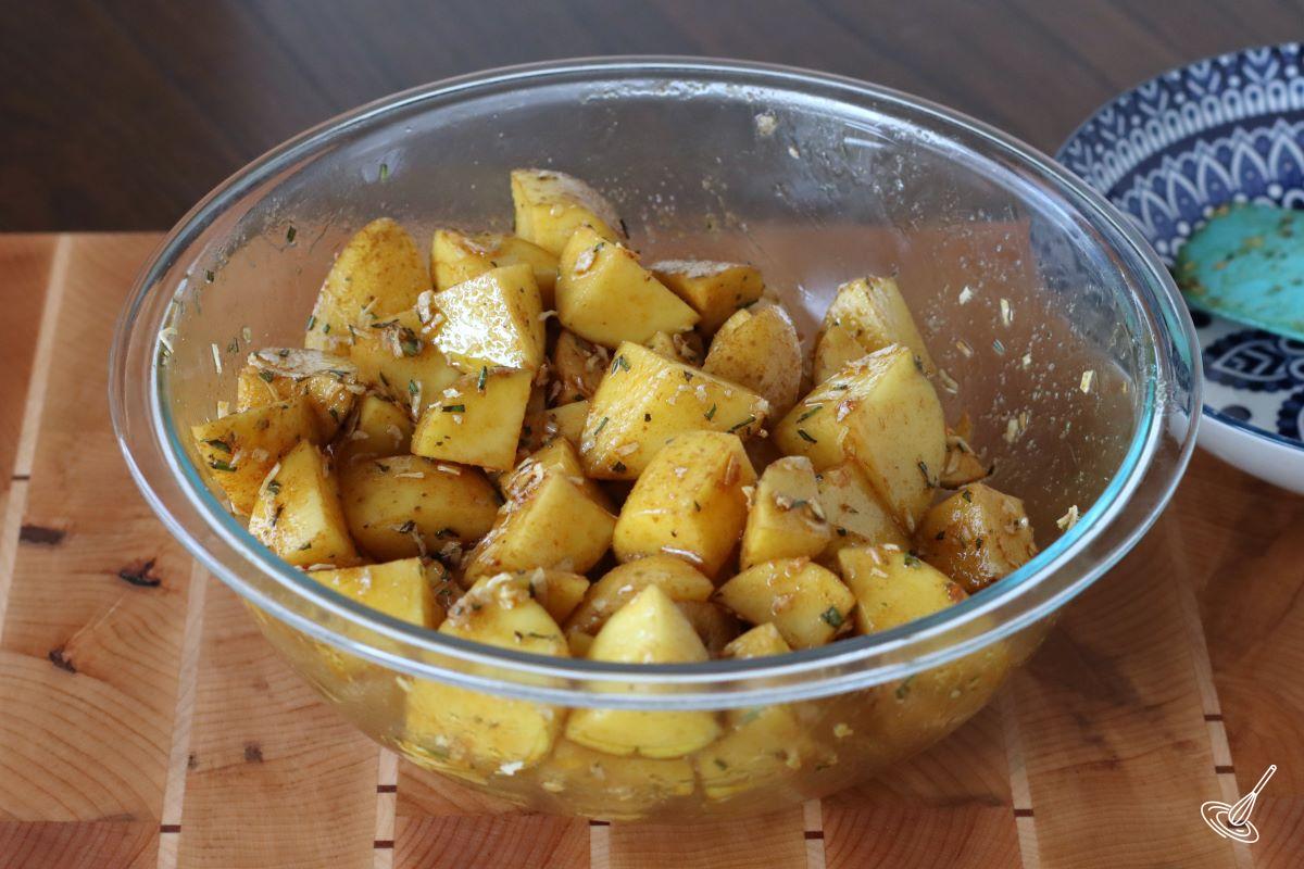 Seasoning cubed potatoes in a large bowl.