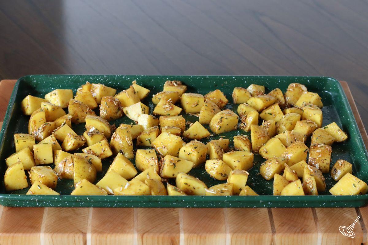 Seasoning cubed potatoes on a baking tray.
