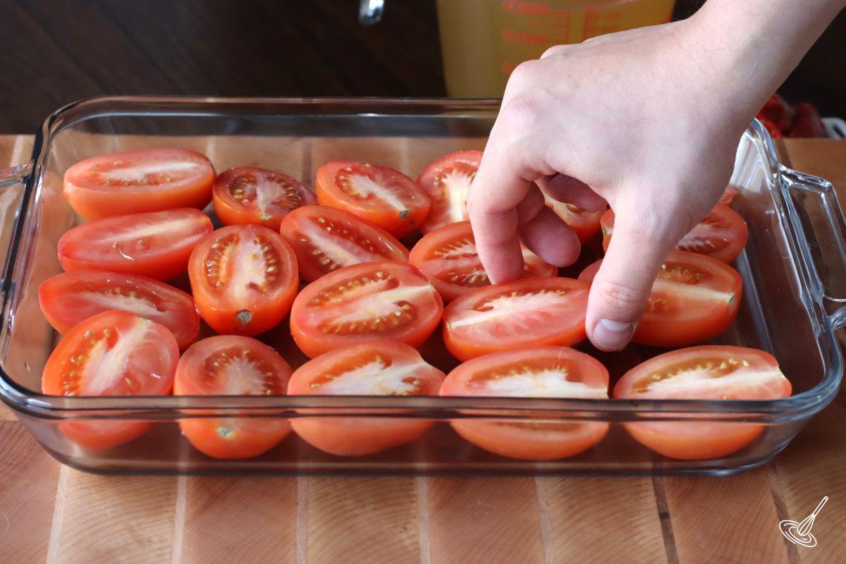 Someone placing halved Toma tomatoes in a baking dish.