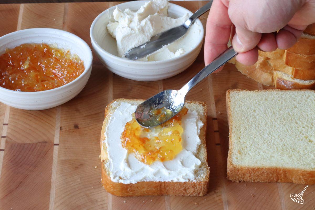 Someone spreading orange marmalade and mascarpone on a slice of brioche bread.