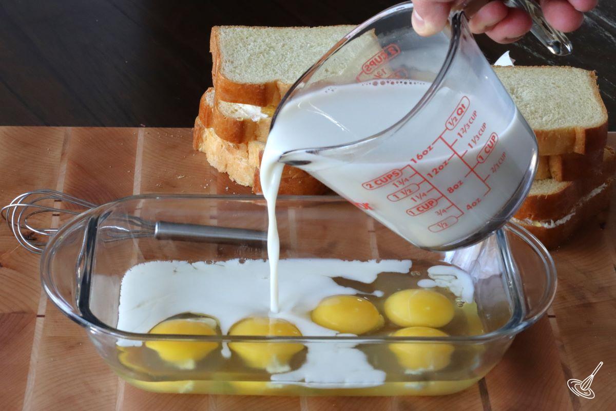 Someone adding milk to a container with eggs.