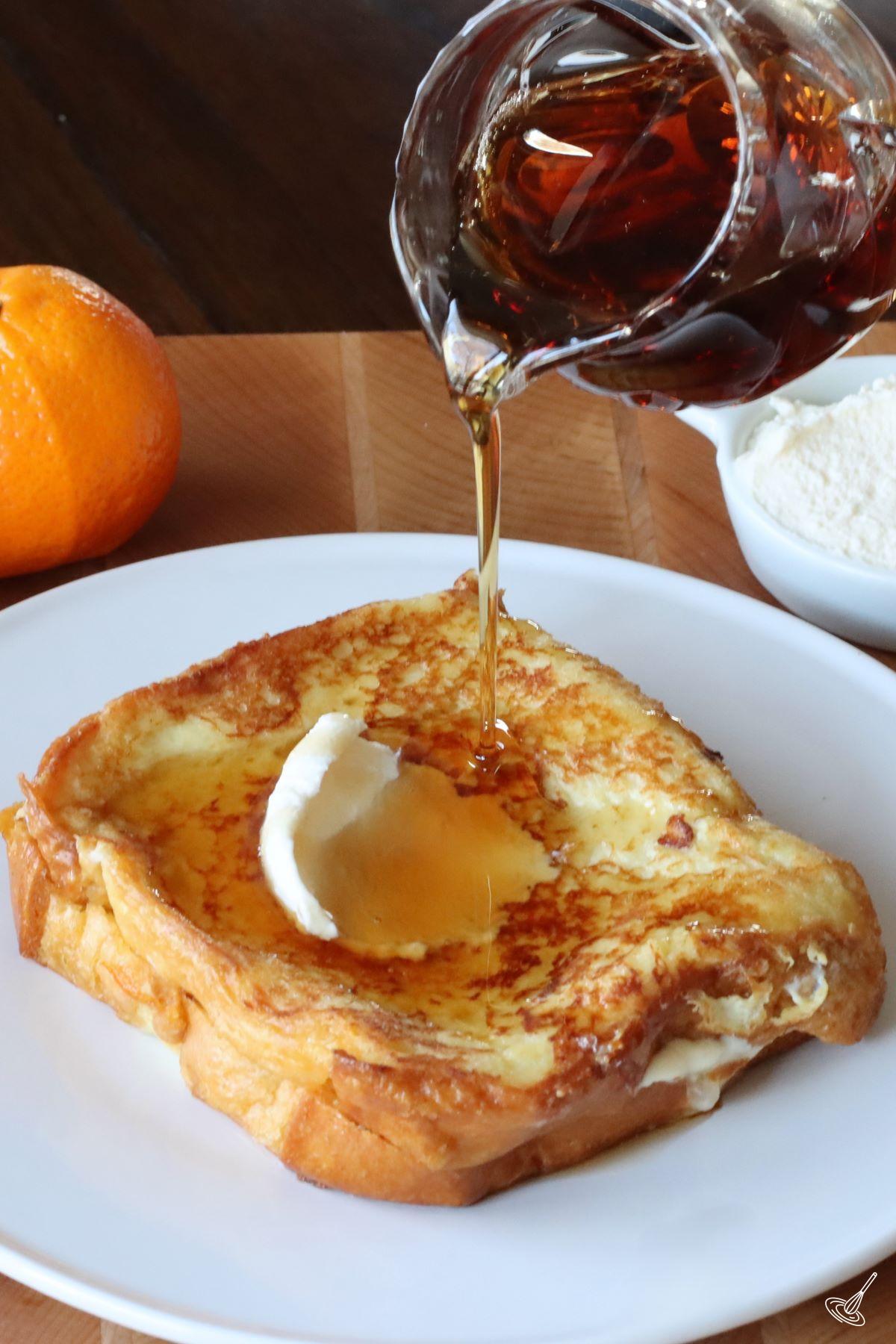 Someone pouring maple syrup on Stuffed Brioche French Toast Orange Marmalade Recipe. 
