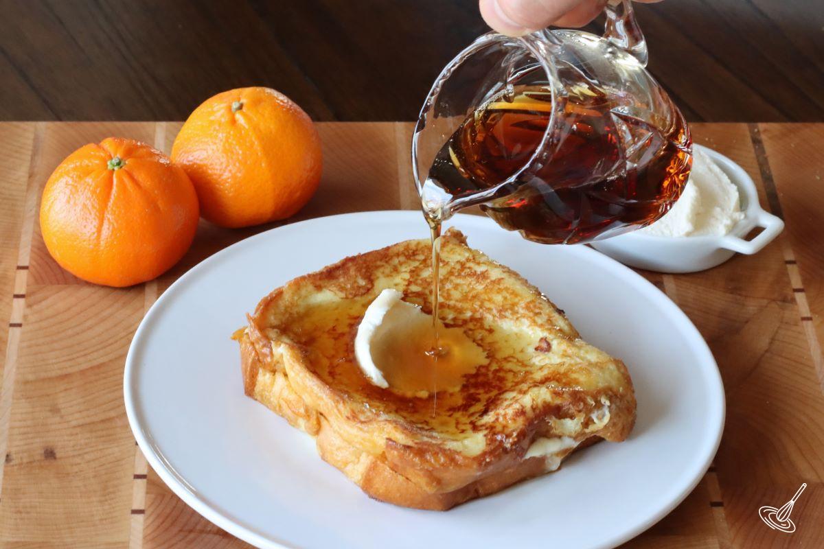 Someone pouring maple syrup on aStuffed Brioche French Toast Orange Marmalade Recipe.