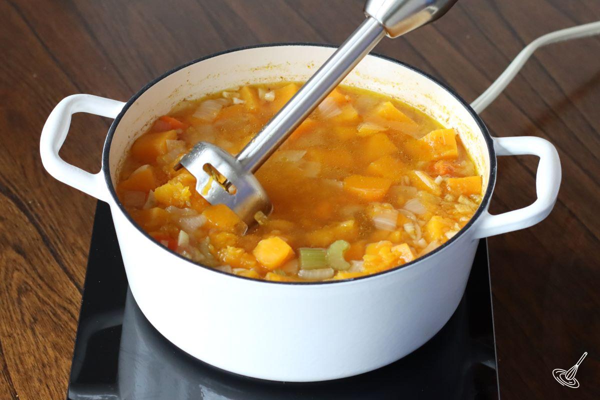 Someone using an immersion blender to blend the Butternut Squash and Potato Soup.