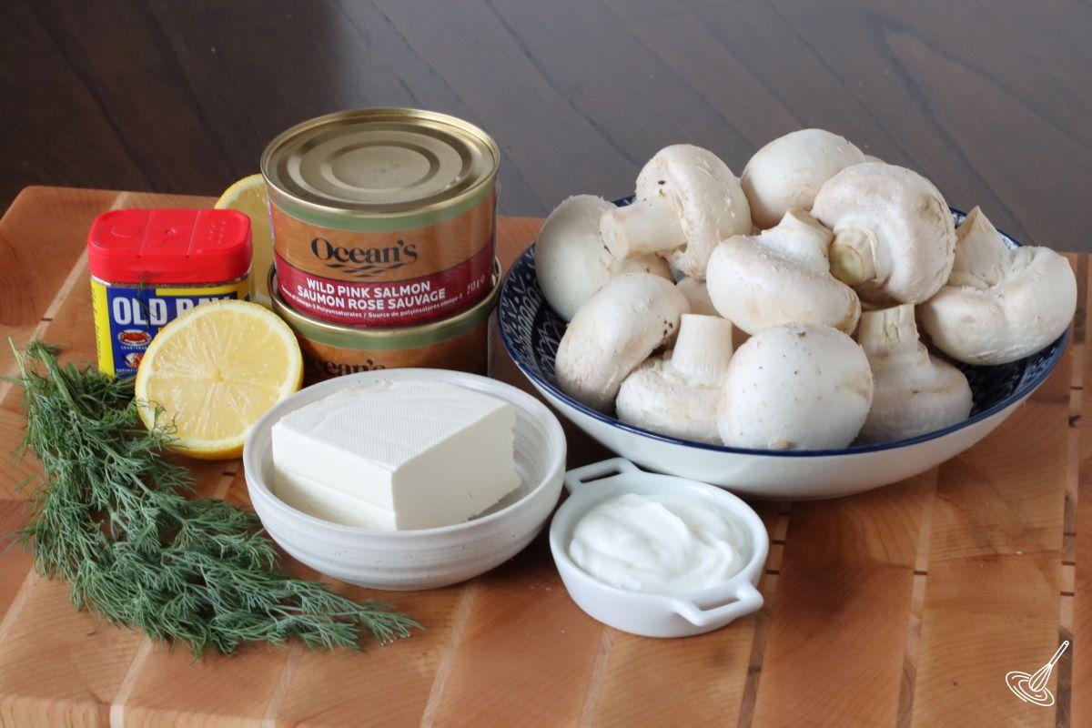 A bowl of white mushroom and cans of salmon on a cutting board.