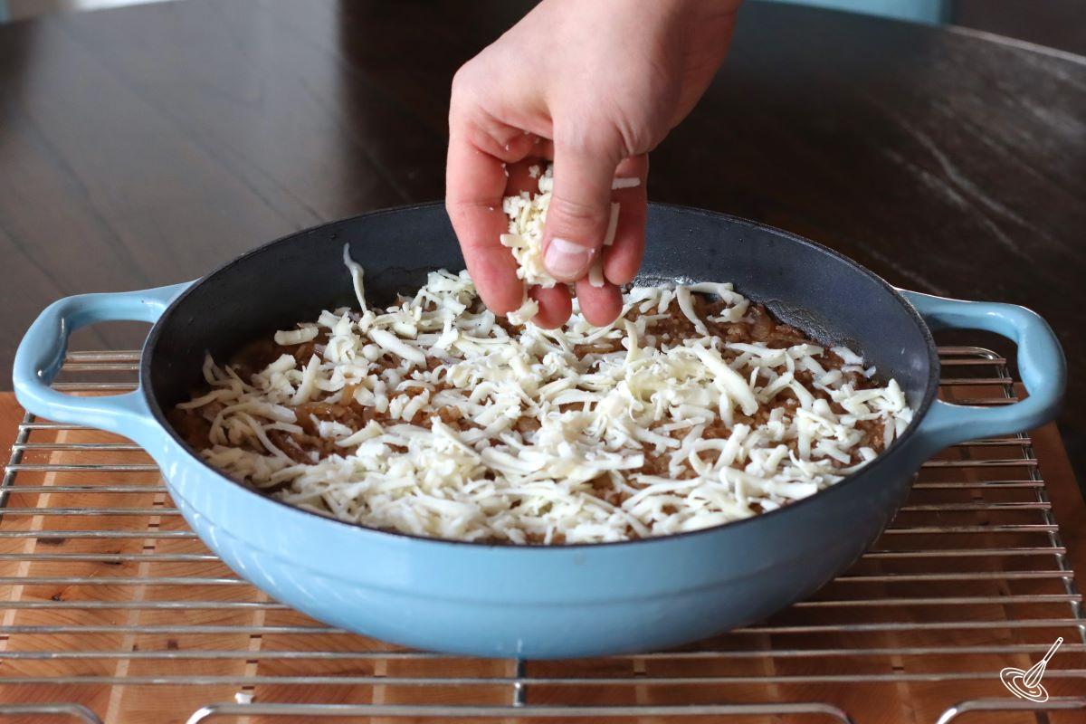Someone sprinkling grated cheese on French Onion Soup Rice.