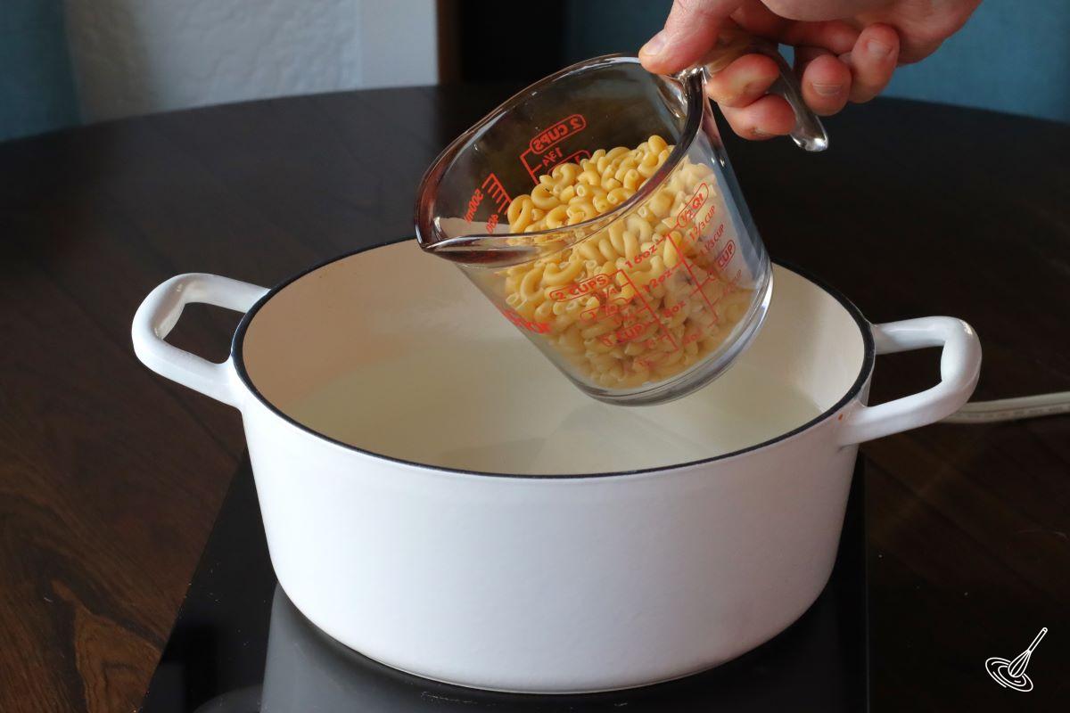 Someone adding elbow macaroni to a pot of boiling water.