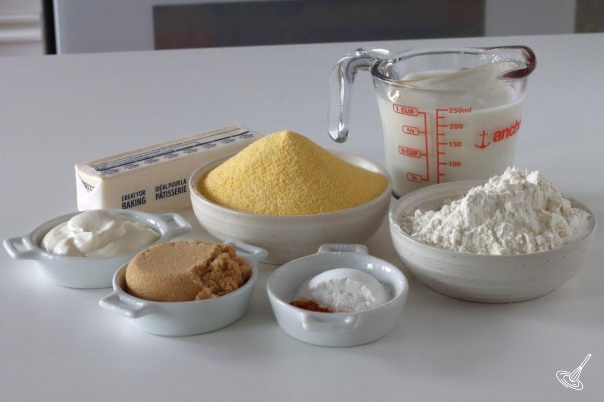 Ingredients to make cornbread, including cornmeal, flour, milk, butter and spices.