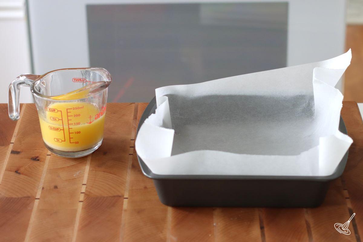 A measuring cup of melted butter, beside a baking tray.