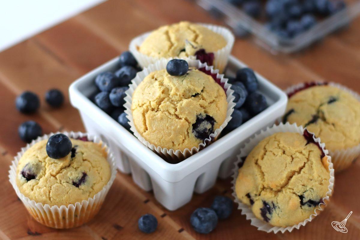 Blueberry Corn Muffins in a container with fresh blueberries. 