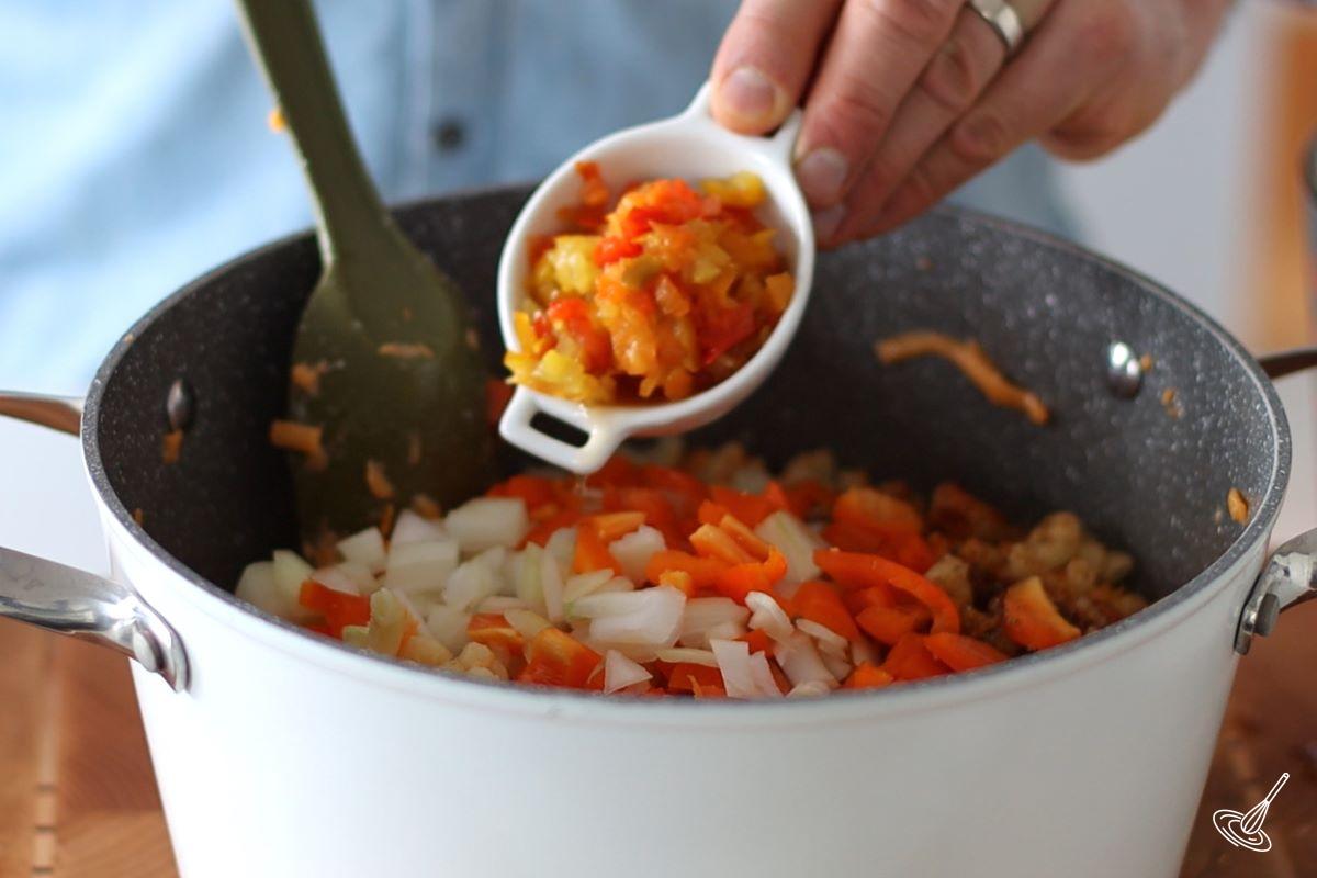 Someone adding chopped pickled banana peppers to a large pot of macaroni and cheese. 