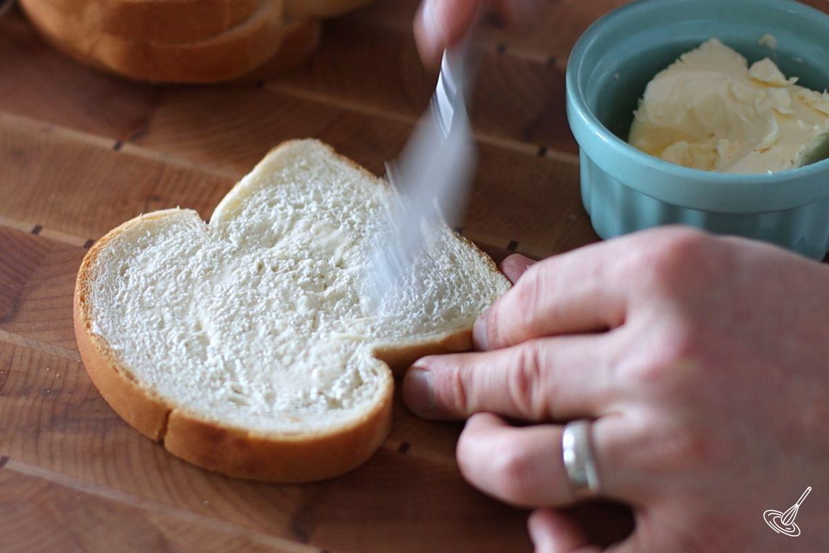 Someone spreading butter on a slice of sandwich bread. 