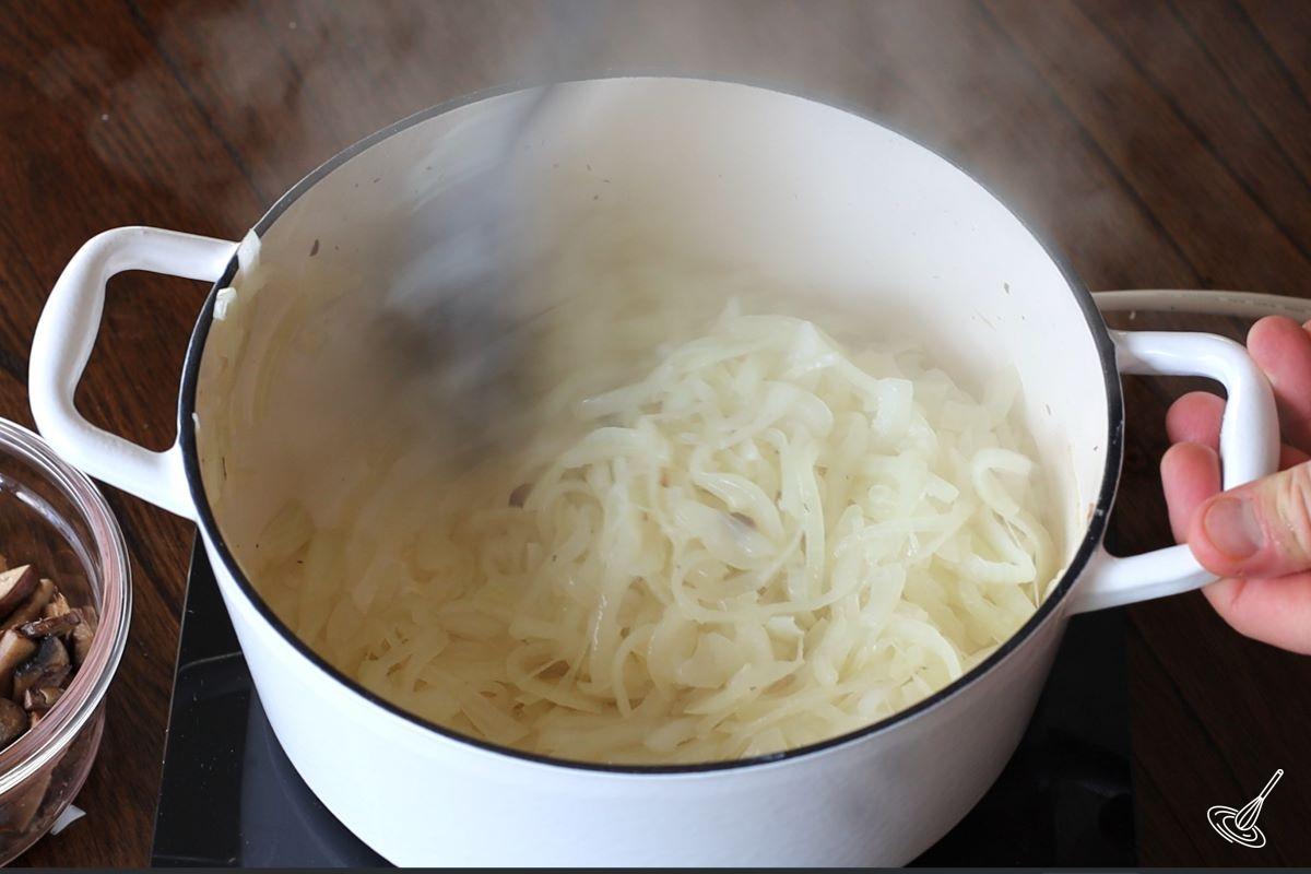Someone stirring cooked onions in a Dutch oven. 