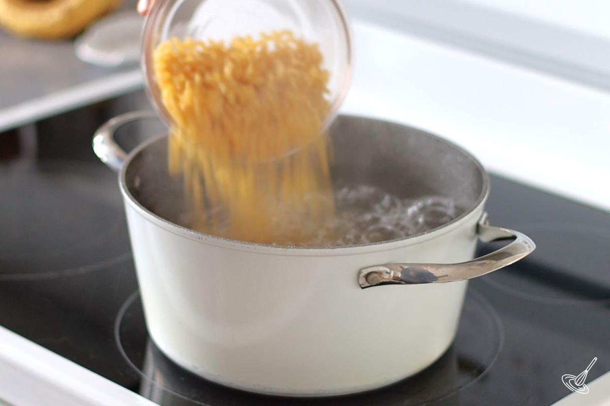 Someone pouring elbow macaroni in a pot of boiling water. 