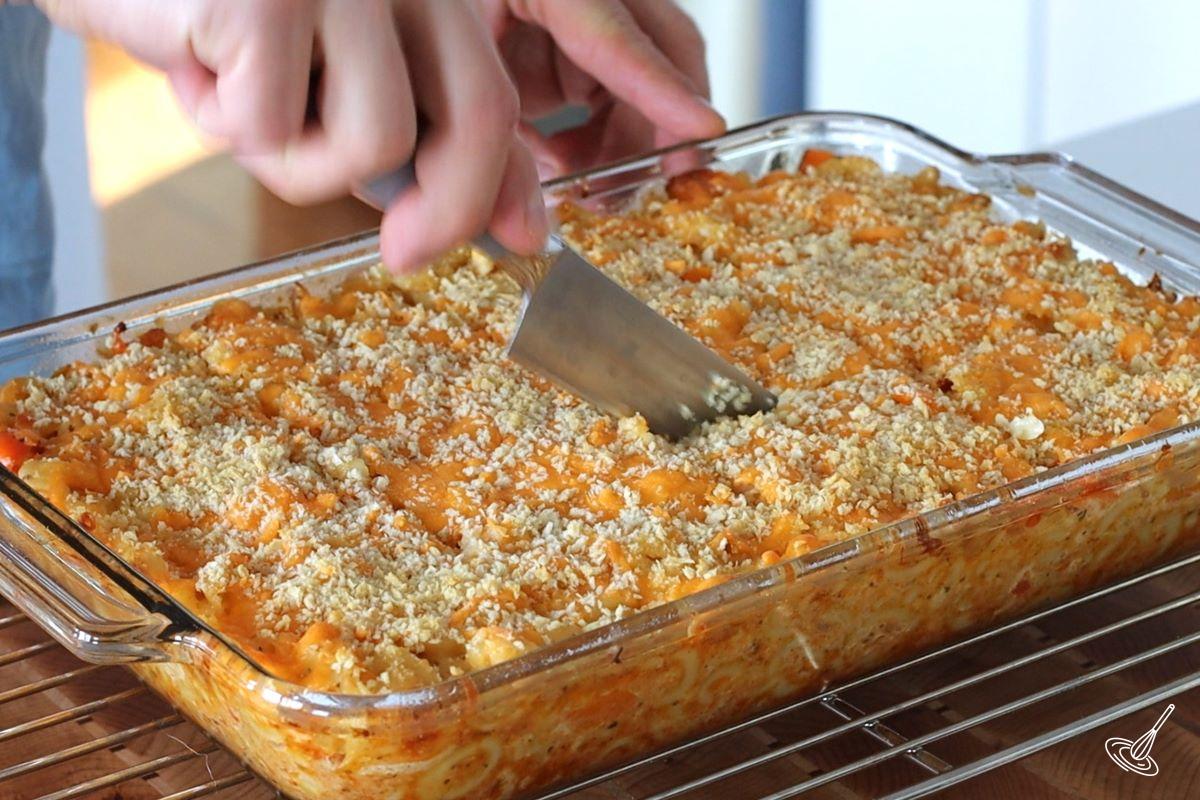 Someone cutting squares of baked Bahamian Mac and Cheese.