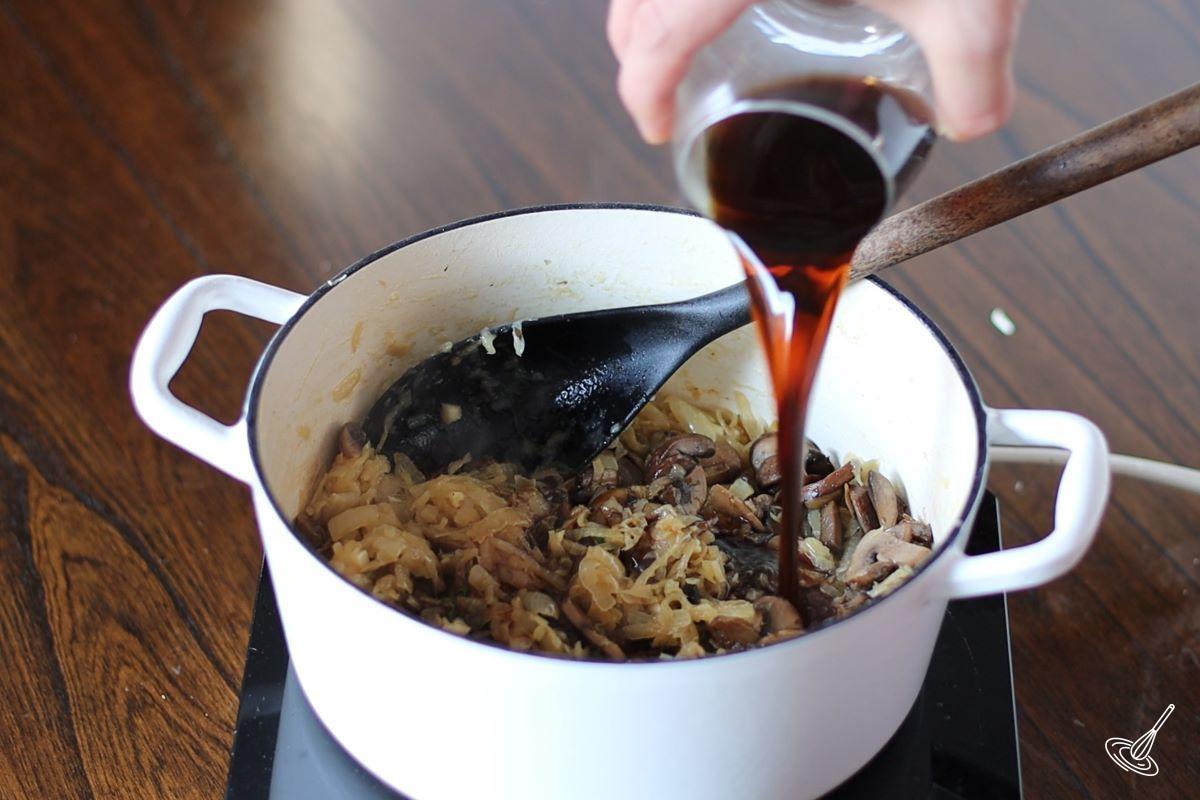 Someone pouring wine in a Dutch oven of onion soup.