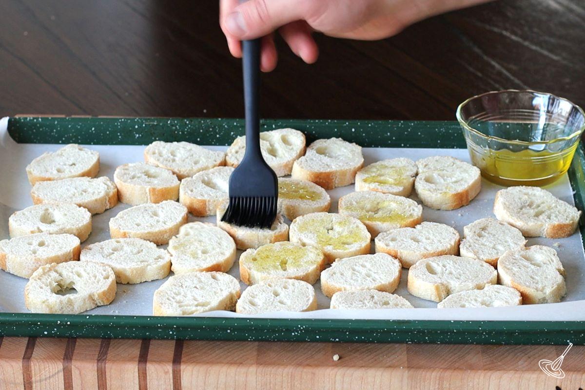 Someone brushing slices of baguette with olive oil.