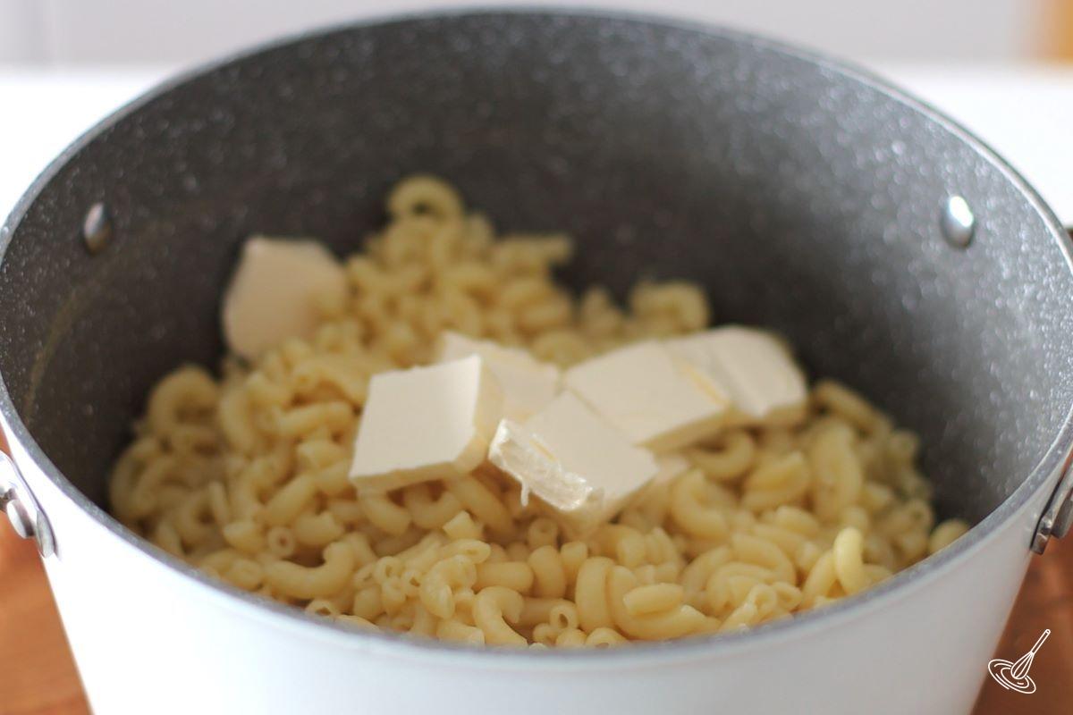 A pot of cooked macaroni with pieces of butter on top. 