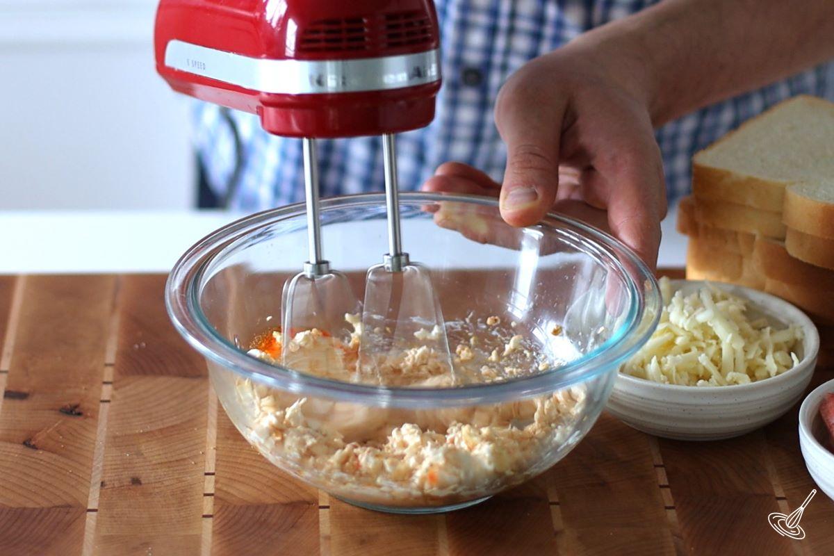 Someone using a hand blender to make a cream cheese filling.