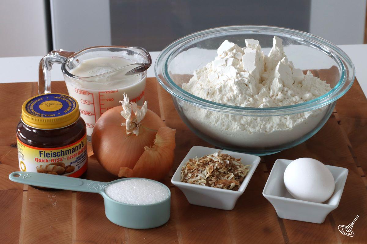 Ingredients to make Soft Onion Rolls, including a bowl of flour, a cup of milk, an egg and onion soup mix.