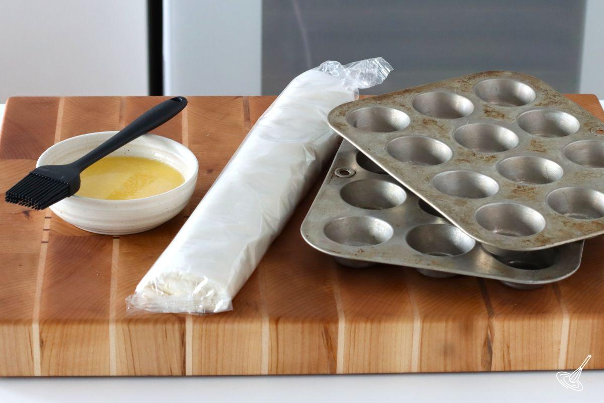 Mini muffin tins with a roll of phyllo dough and a container of melted butter.