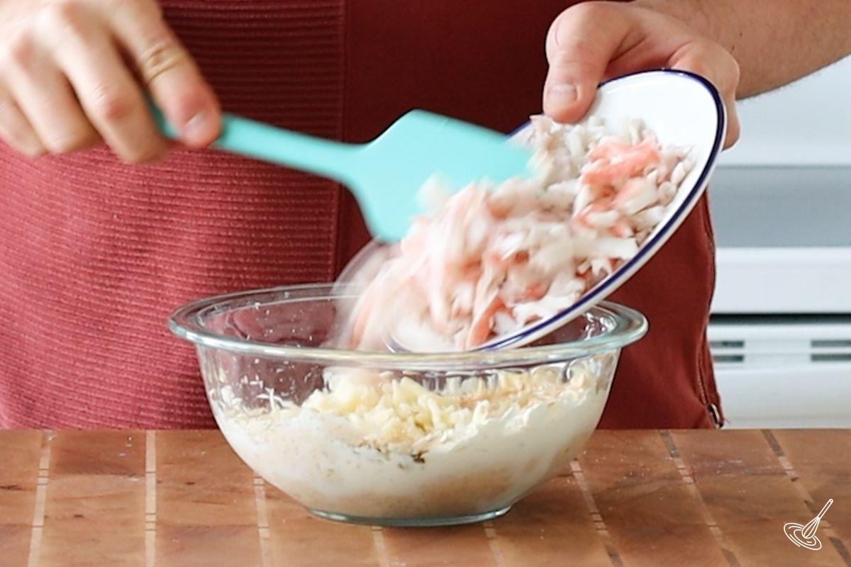 Someone adding pieces of imitation crab to a bowl of cream cheese.