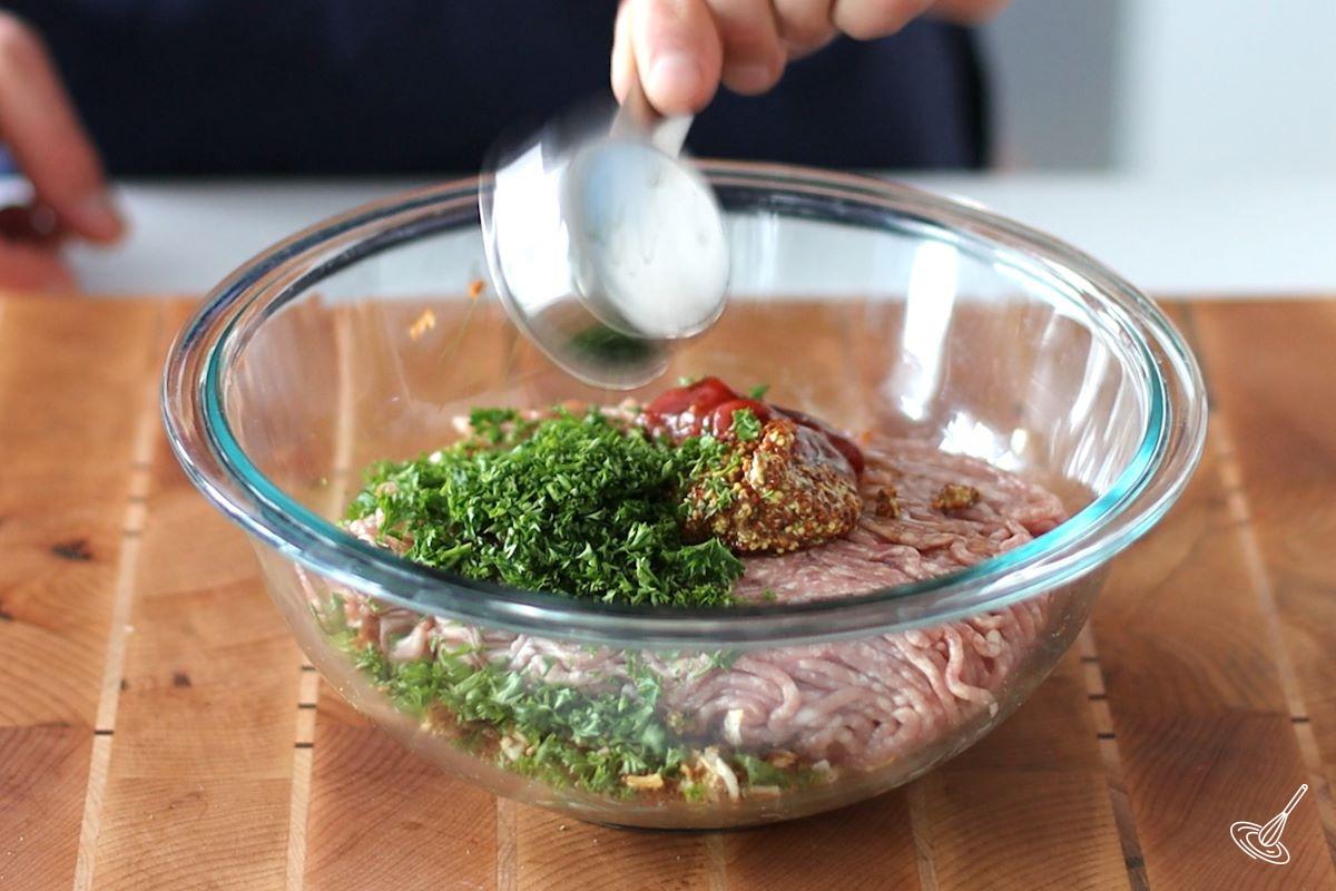 Someone adding fresh parsley to a large bowl of ground pork and seasoning.