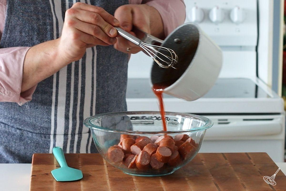 Someone pouring Maple BBQ sauce on Hasselback Kielbasa Bites.