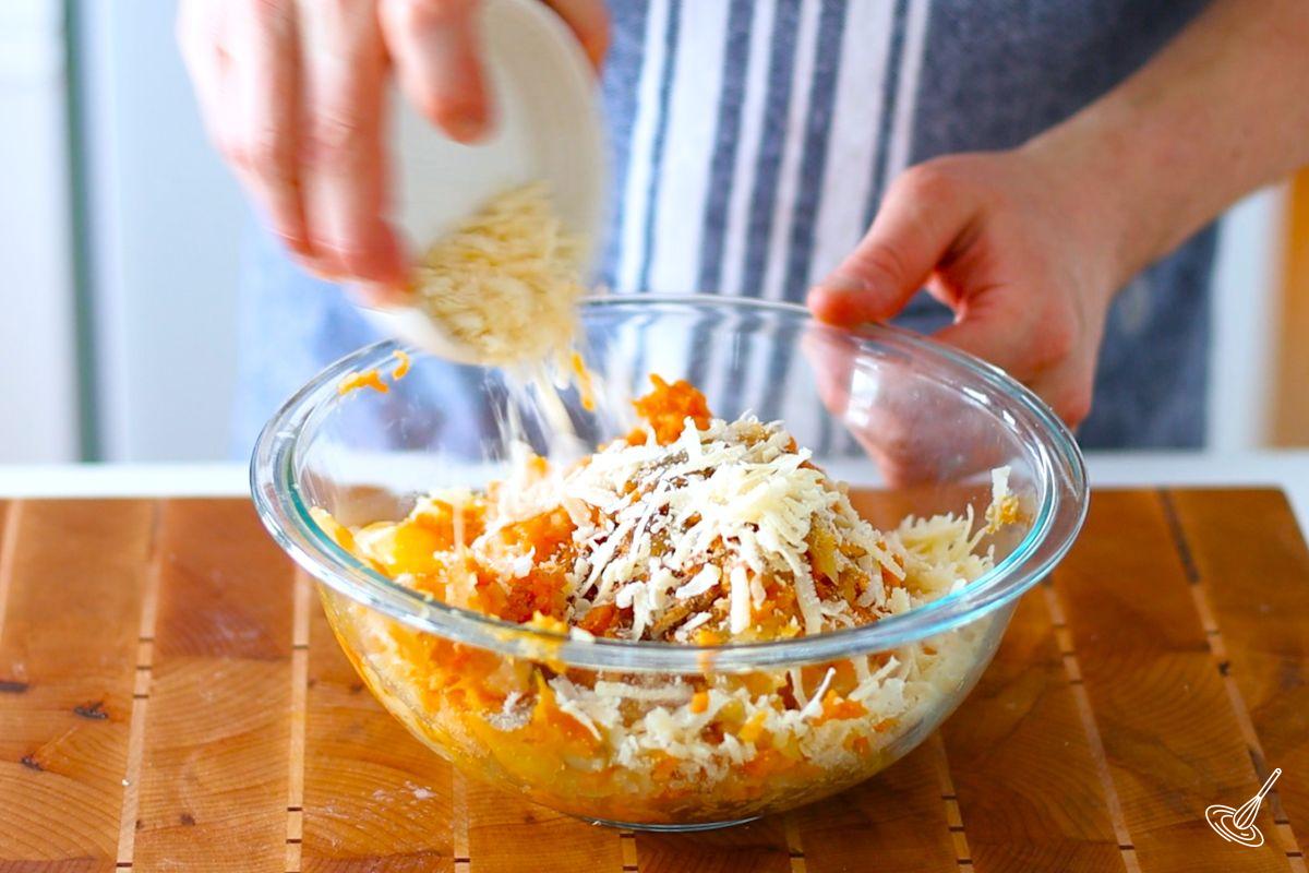 Someone adding grated parmesan cheese to a large bowl of mashed potatoes.