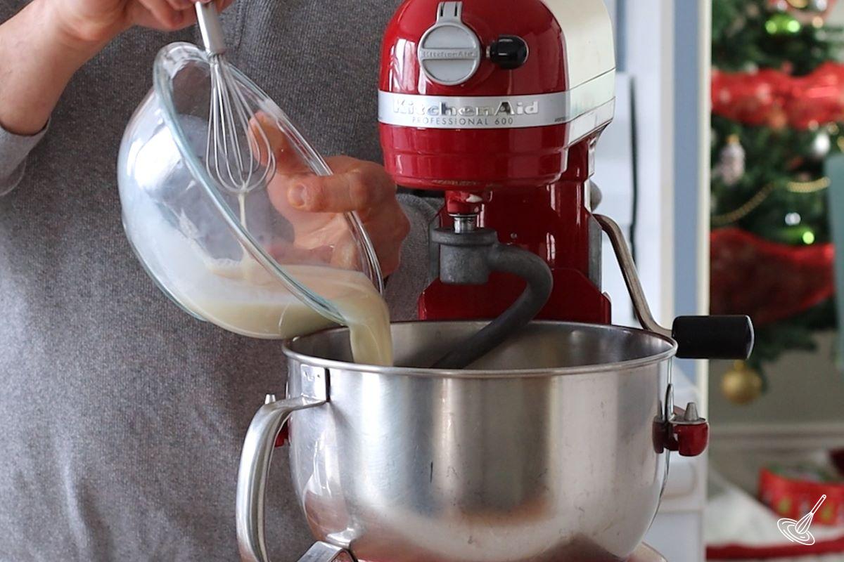 Someone pouring wet ingredients in a bowl of a stand mixer.