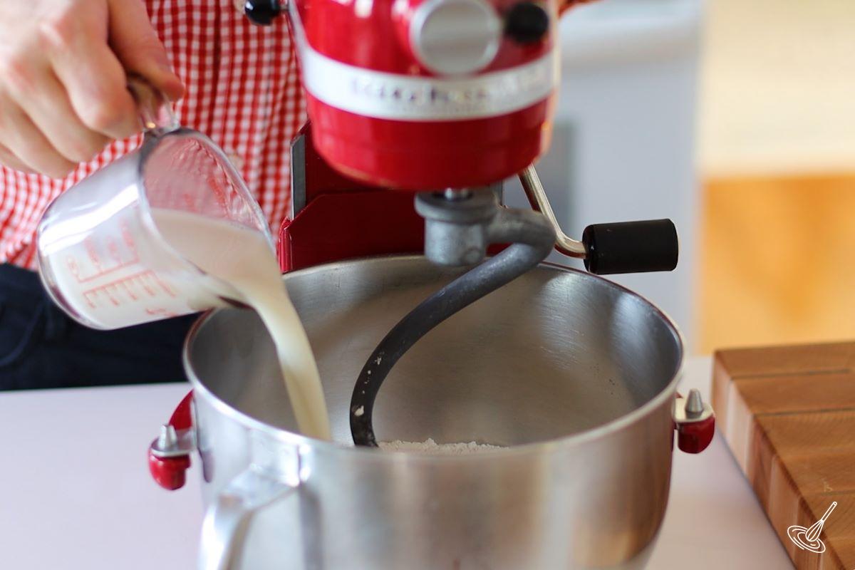 Someone adding wet ingredients to a stand mixer.