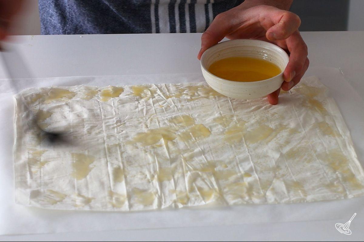 Someone brushing melted butter on a sheet of phyllo pastry.