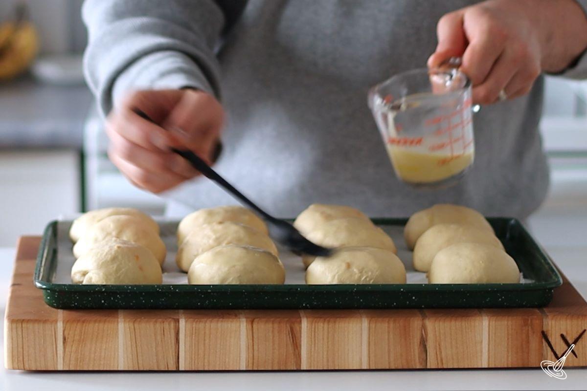 Someone brushing soft onion rolls with egg wash